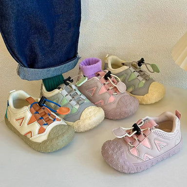 Tre par barnsneakers utan skosnören i vit, rosa och ljusgrön bredvid barnfot