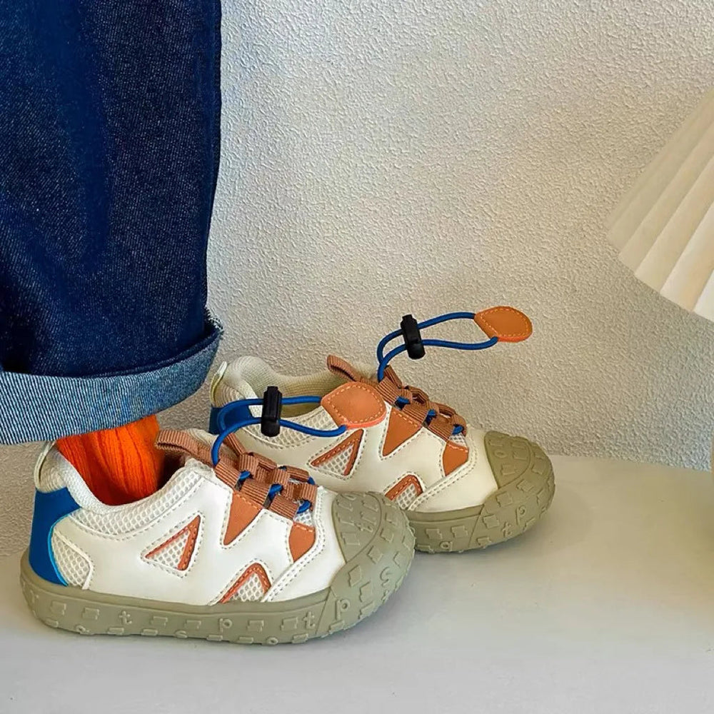 Vita barnsneakers med orange detaljer på barnfot, sedda från sidan